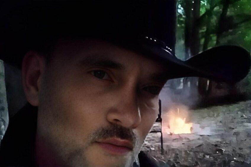 A person wearing a hat, a campfire, and a forested background. 5
