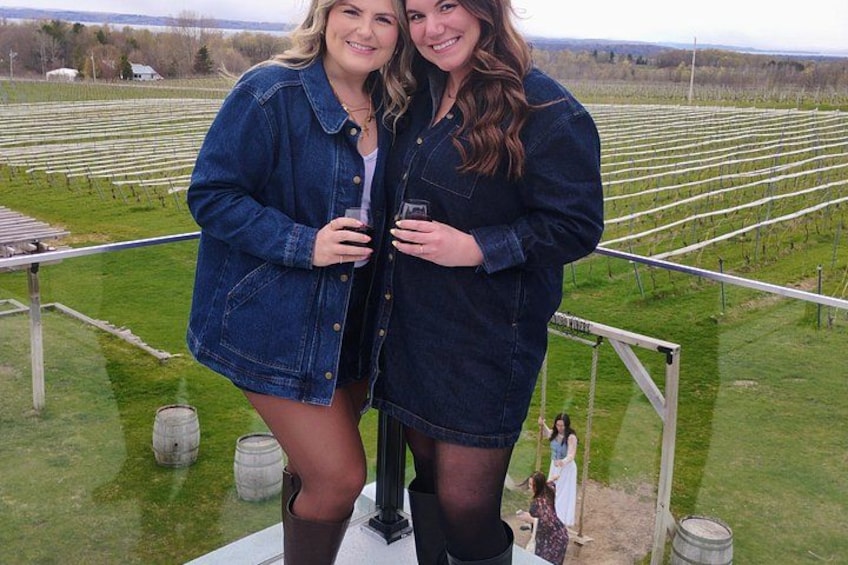 Two people standing on a platform in a vineyard with rows of grapevines. 2
