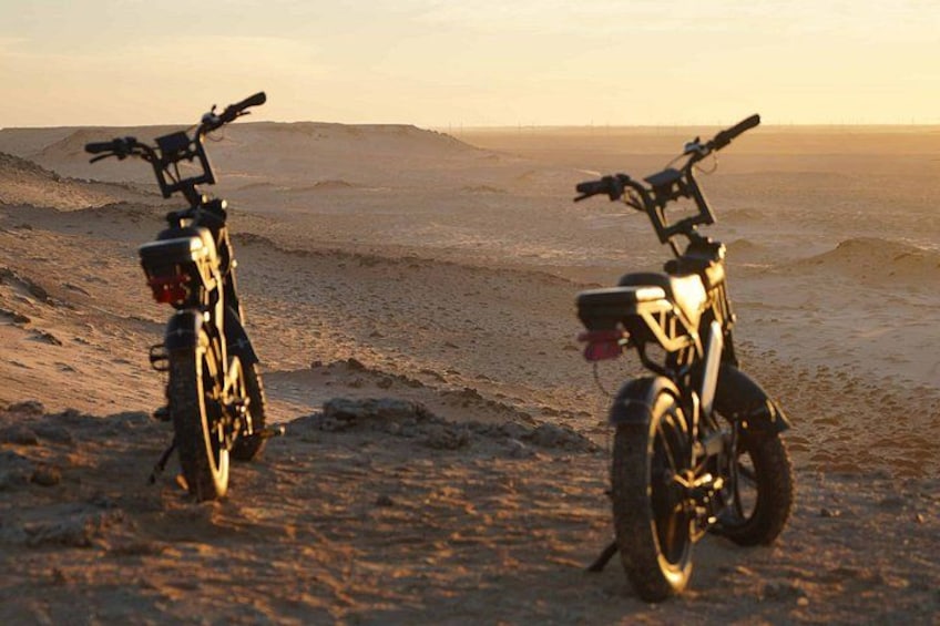 To motorcykler parkeret på en sandstrand med solnedgang i baggrunden. 2