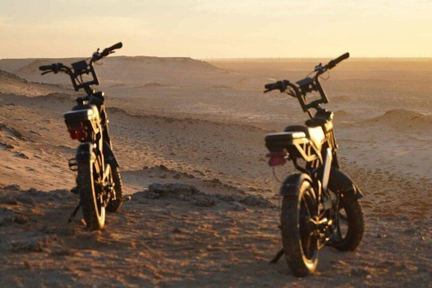 Two motorcycles parked on a sandy beach with a sunset in the background. 1