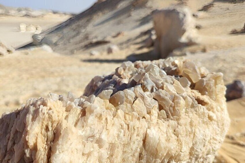 Eine Nahaufnahme einer großen, beige gefärbten Felsformation mit rauer Oberfläche, eingebettet in eine Wüstenlandschaft. 4