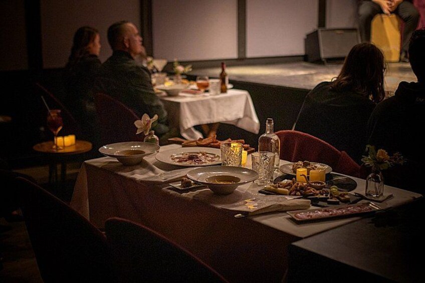 A dimly lit dining area with tables set for a meal, candles, and various dishes. 4