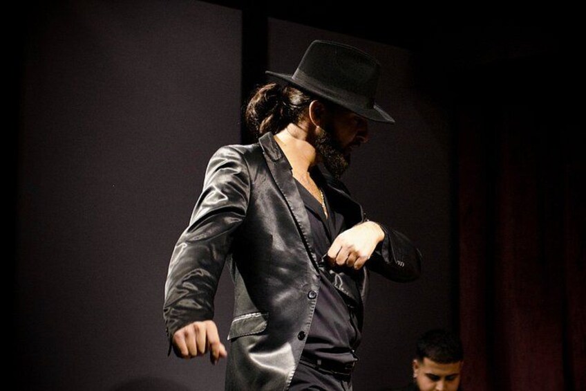 A person in a dark suit and hat walking indoors. 2