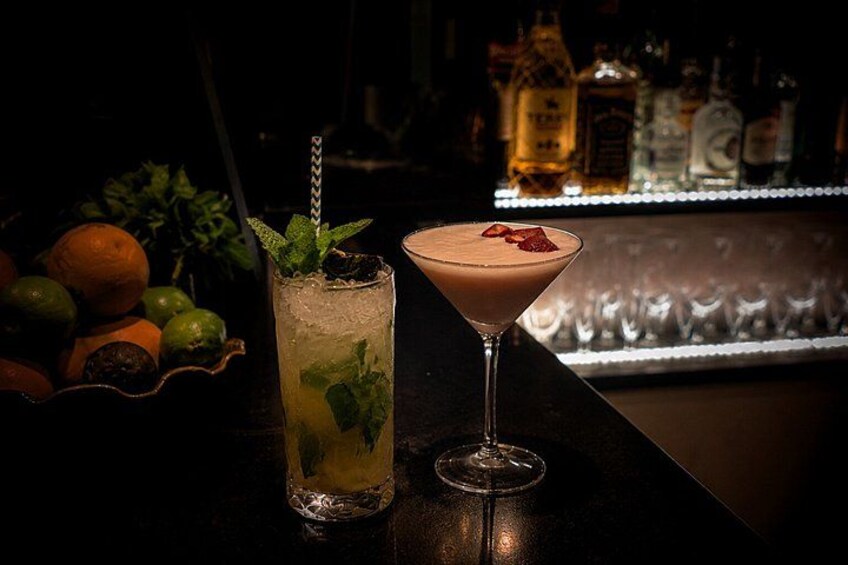 Two drinks on a bar counter with a bottle in the background. 3