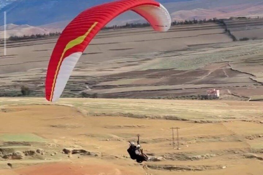 Een persoon zweeft met een rode en witte parachute boven een glooiend landschap. 1