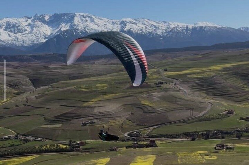 Een paraglider met een rood-wit parachutefluistert over een bergachtig landschap met besneeuwde toppen in de verte. 3