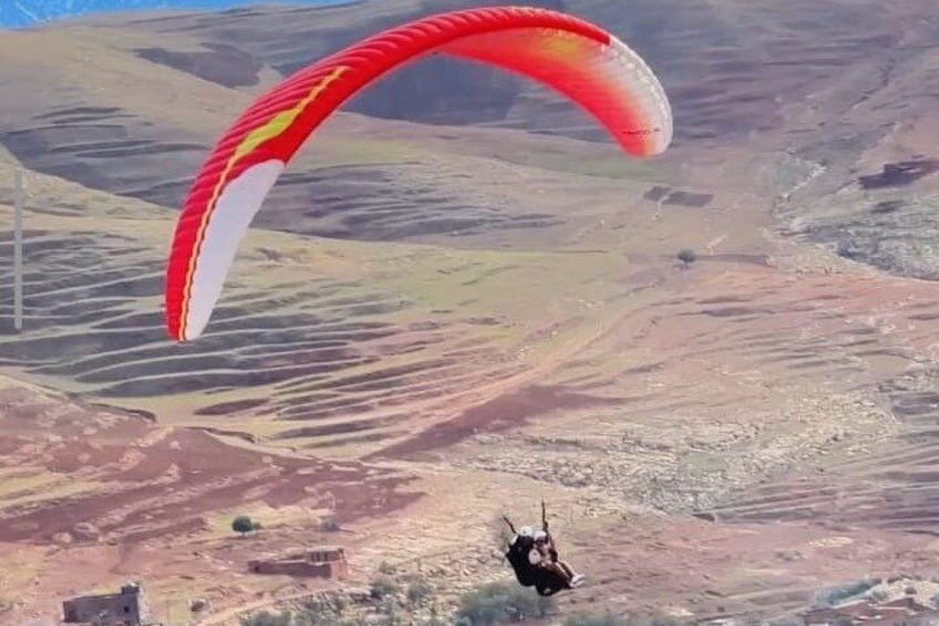 Een persoon paraglide boven een kaal landschap met glooiende heuvels. 2