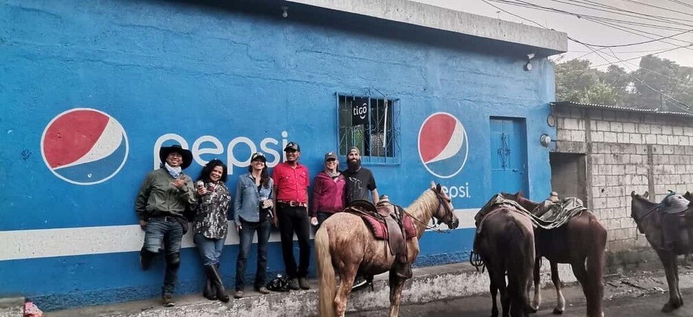 A group of people standing in front of a blue wall with Pepsi logos, with a horse and a cart nearby. 2