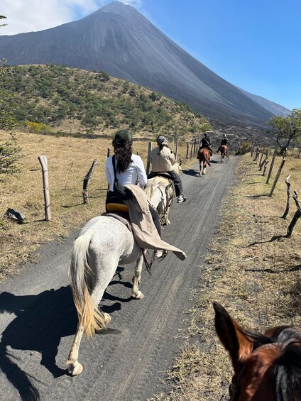 A group of people horseback riding on a road with a mountain in the background. 4