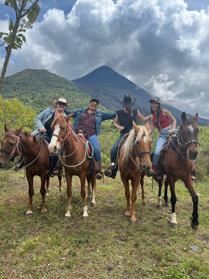 Four people riding horses in a grassy field with a mountain in the background. 1