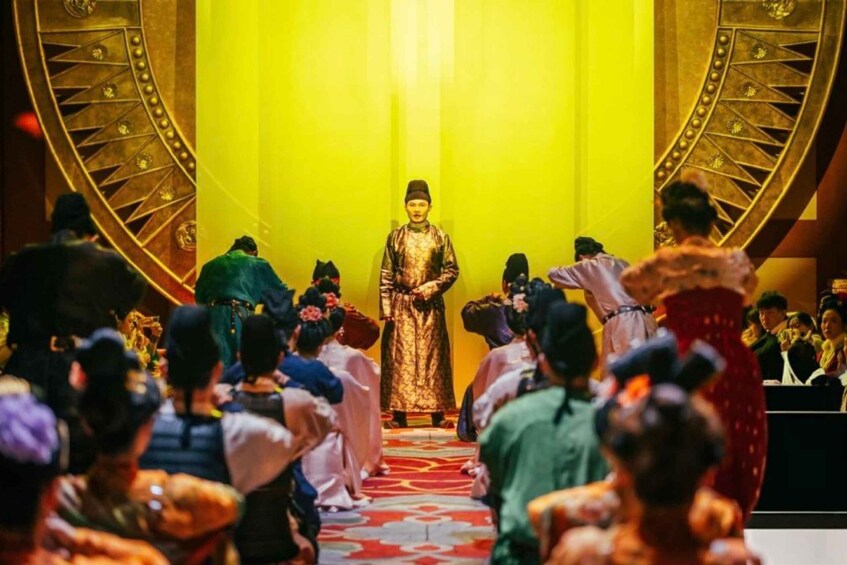 A person in traditional attire standing on a stage with a crowd in front. 2