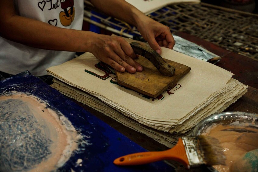 A person using a wooden mallet to press a design onto paper. 4