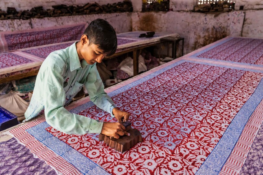 A person working on a large, patterned textile on the floor. 5