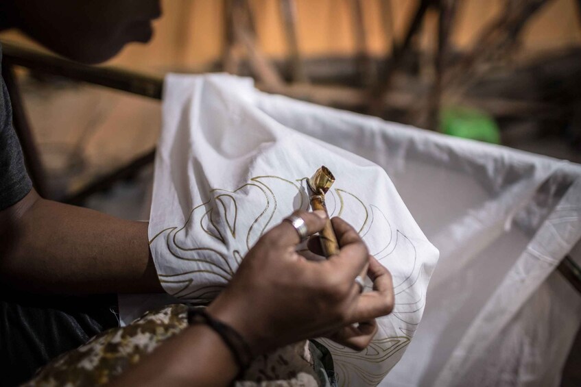 A person sewing with a needle and thread on a white fabric. 3