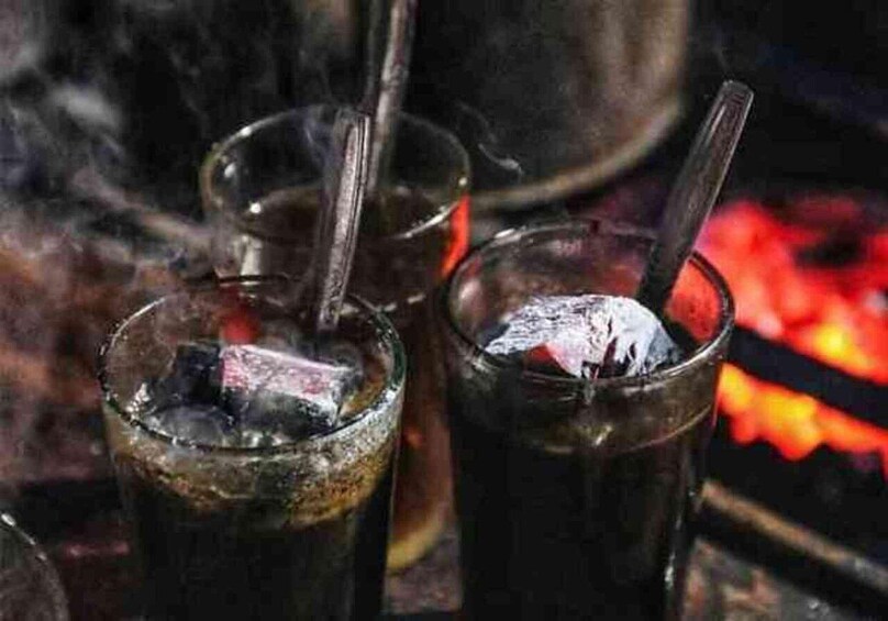 Two glasses of dark liquid with ice cubes and straws, placed near a fire. 4