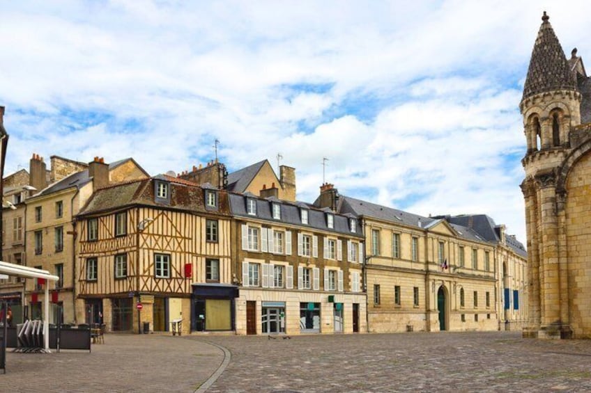 A cobblestone street with historic buildings, including a half-timbered structure and a church tower. 5
