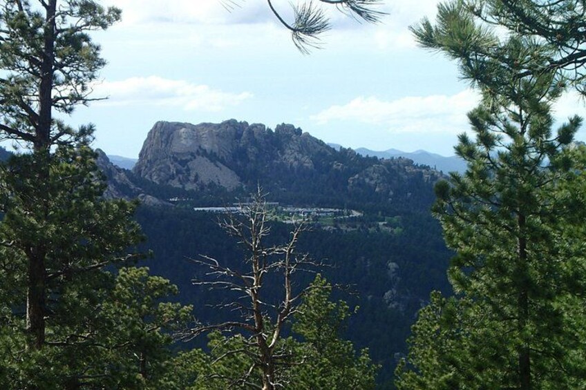 Paesaggio montano con una cima rocciosa imponente, circondata da una fitta foresta e un cielo sereno. 3