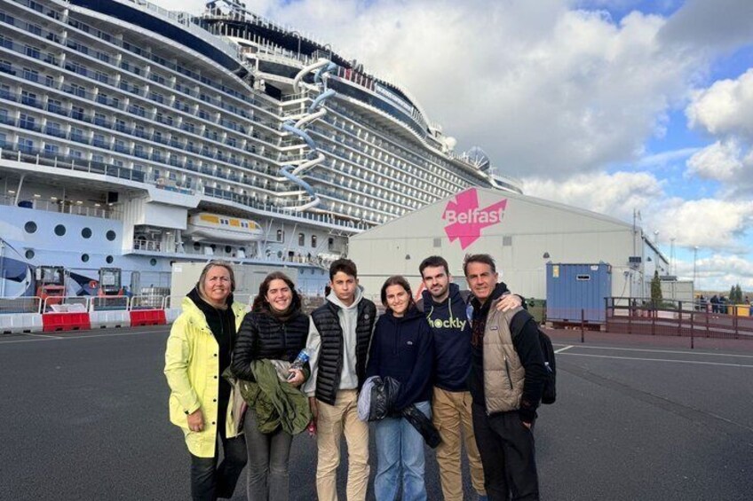 Un groupe de personnes se tient devant un navire de croisière, sur lequel on peut voir une pancarte indiquant « Belfast ». 1
