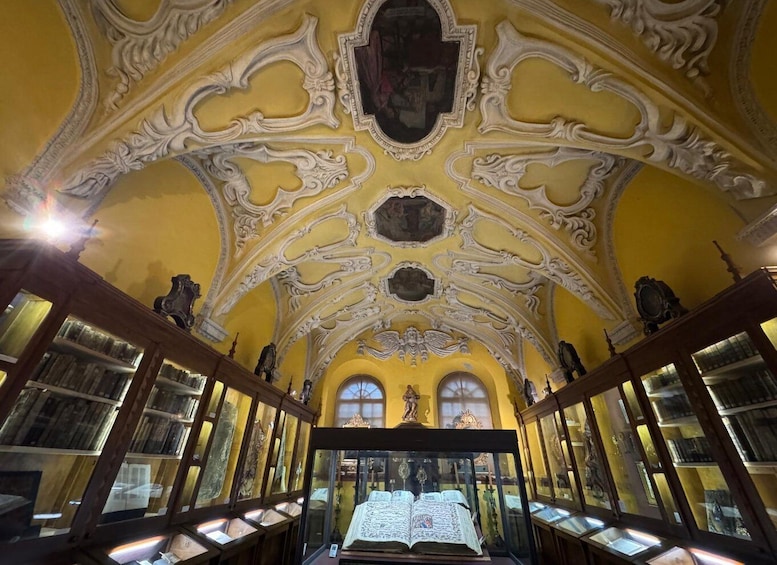 An ornate library interior with yellow walls, intricate ceiling designs, and glass display cases. 5