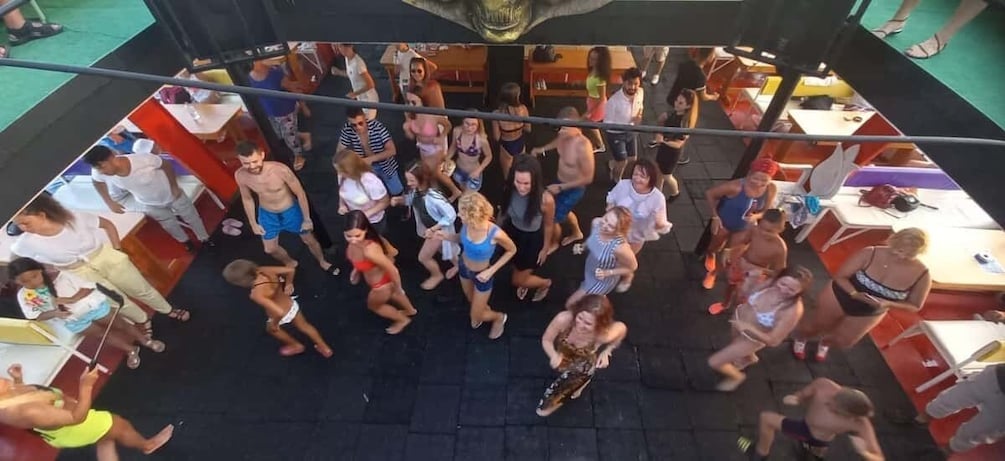 A group of people gathered on a boat deck, some standing, some sitting, with tables and chairs around. 4