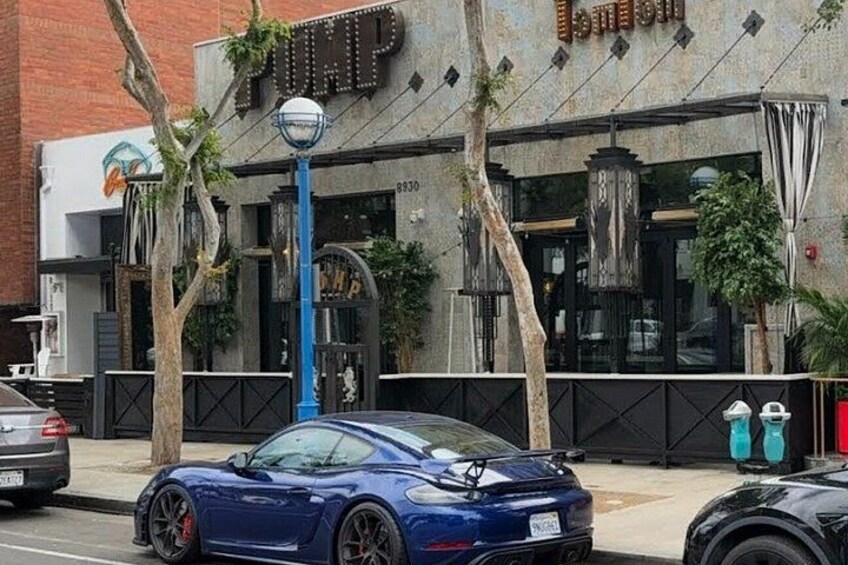 Un'auto sportiva blu parcheggiata di fronte a un edificio con un cartello che riporta la scritta 'PUMP'. 2