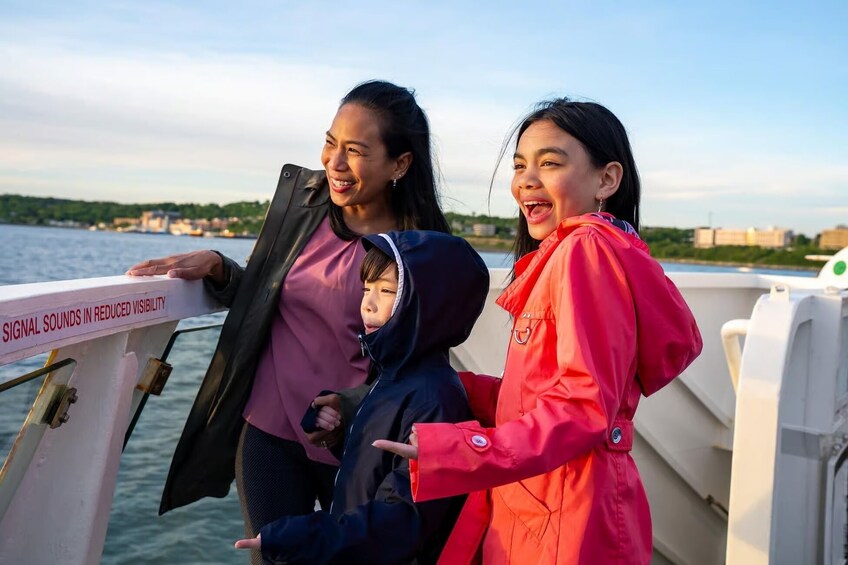 Drei Personen in einem Boot, im Hintergrund eine Stadtlandschaft und Wasser. 4