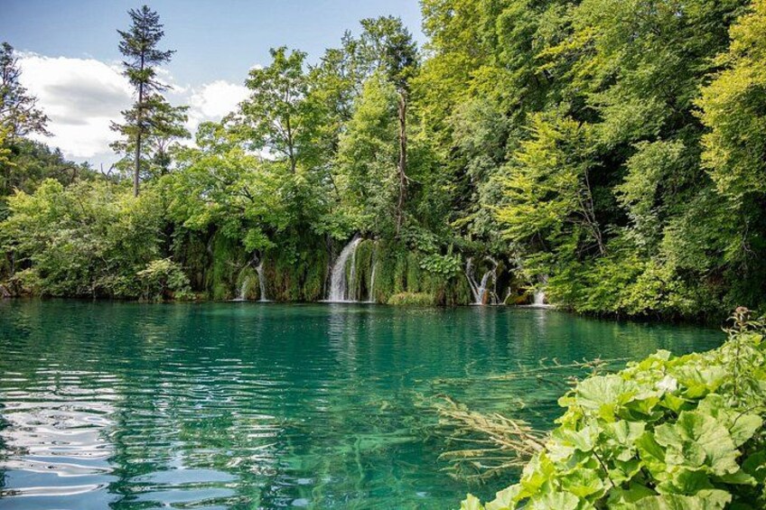 A clear turquoise lake surrounded by lush greenery and waterfalls. 5