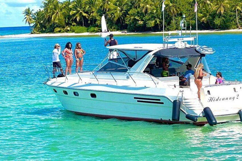 Un barco blanco llamado 'Hidcana2' sobre aguas turquesas, con gente en la cubierta y una playa con palmeras al fondo. 3
