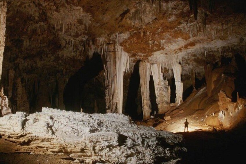 Una cueva con estalactitas y estalagmitas, una persona parada en un saliente, y una abertura de cueva. 2