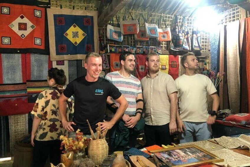 A group of people in a market with textiles and crafts on display. 5