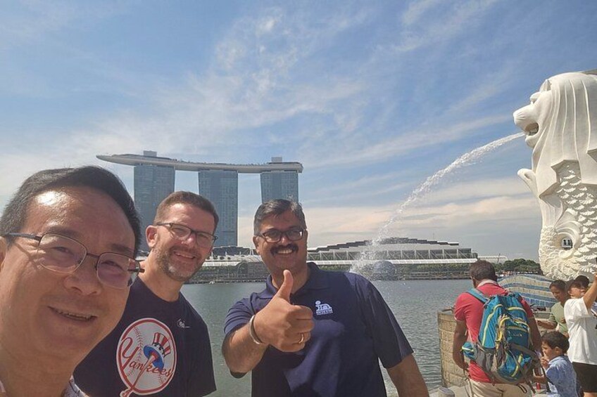 Trois personnes posent devant une grande fontaine et un monument architectural remarquable. 3