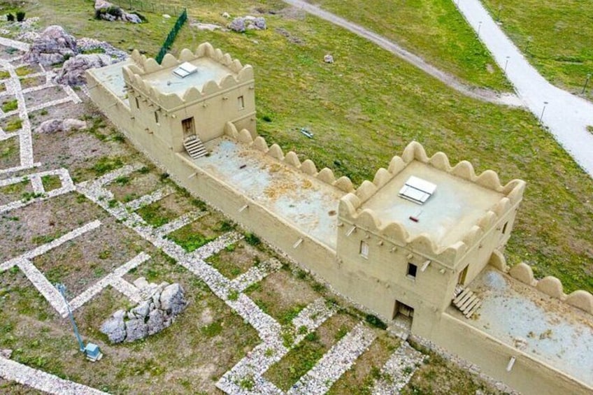 A model of a castle with a square tower and a rectangular building, surrounded by a stone wall and a grassy area. 1