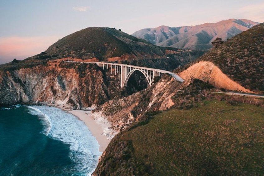 A bridge over a canyon with a beach and mountains in the background. 2