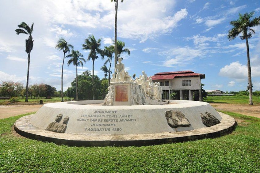 A monument with a statue, surrounded by palm trees and a building with a red roof. 3