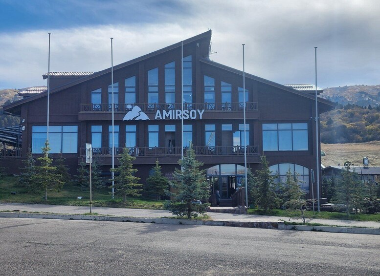 A modern building with the name 'AMIRSOY' and a mountain logo, surrounded by trees and a clear sky. 2