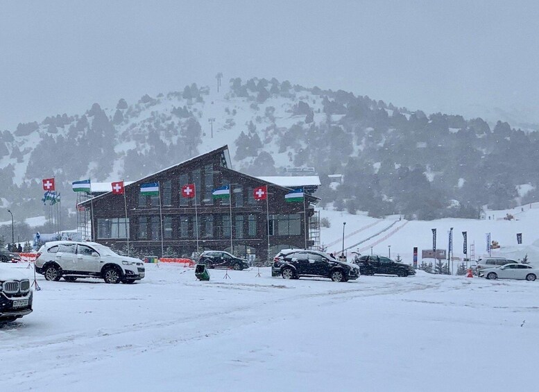 A snow-covered building with flags, cars parked in front, and a snowy mountain in the background. 5