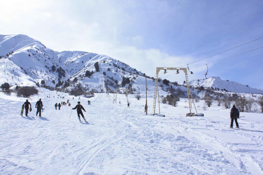 A snowy ski slope with skiers, a ski lift, and a mountain backdrop. 3