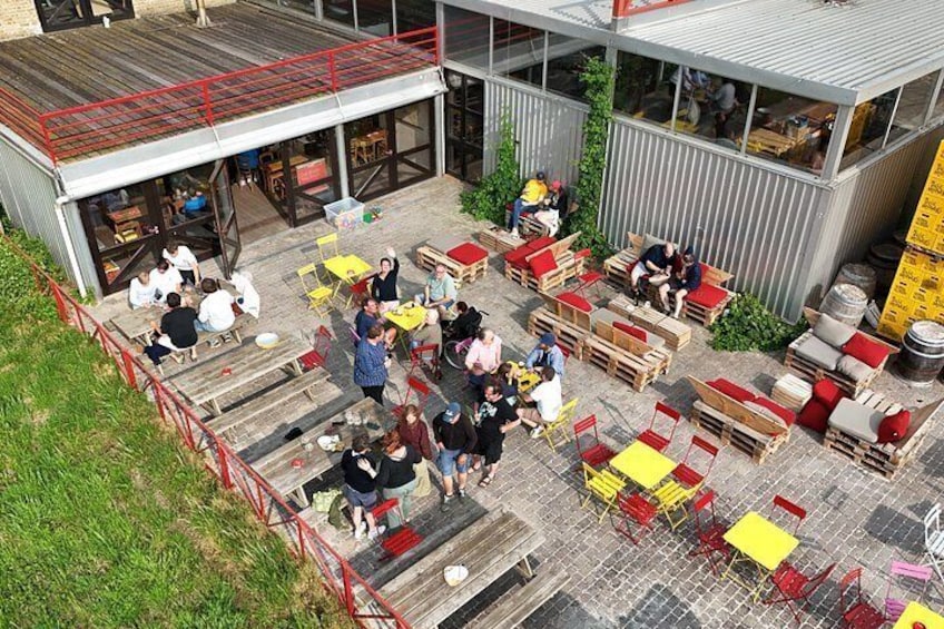 An outdoor seating area with tables and chairs, surrounded by a building with large windows and a red railing. 2
