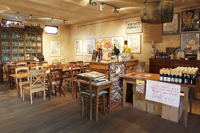 A cozy restaurant interior with wooden furniture, a counter displaying food items, and various artworks on the walls. 5