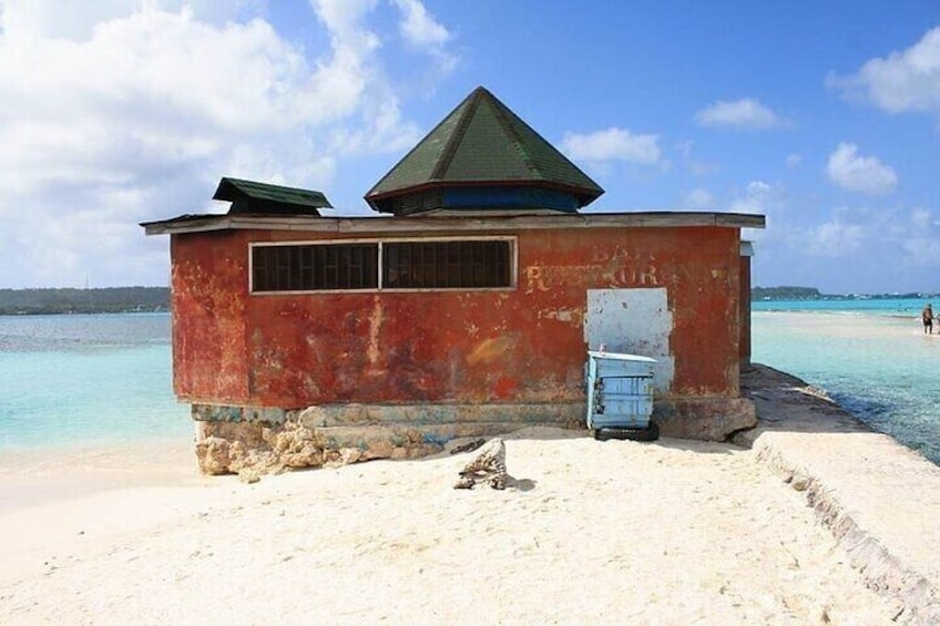 Ein kleines, rotes Gebäude mit einem grünen Dach an einem sandigen Strand. 5