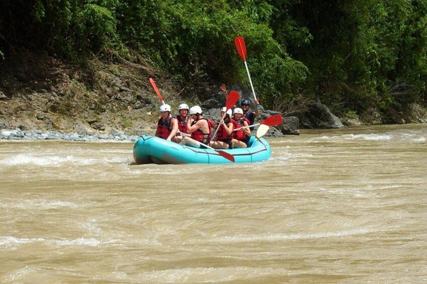 A group of people in a blue raft navigating a river surrounded by greenery. 1
