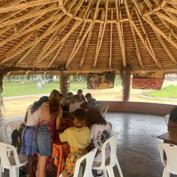 A group of people seated at a table under a thatched roof structure. 2