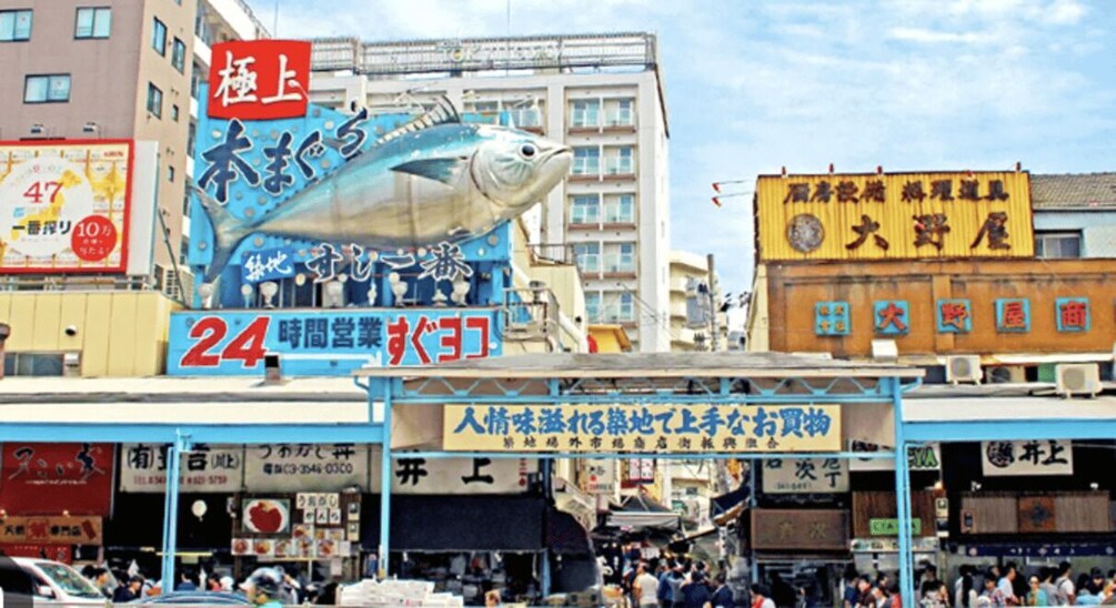A busy street with a large fish sculpture, various shops, and signs in Japanese. 1