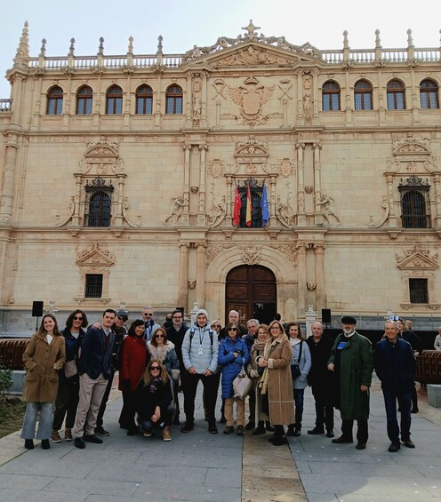 A group of people standing in front of a historic building with ornate architecture and a large door. 1