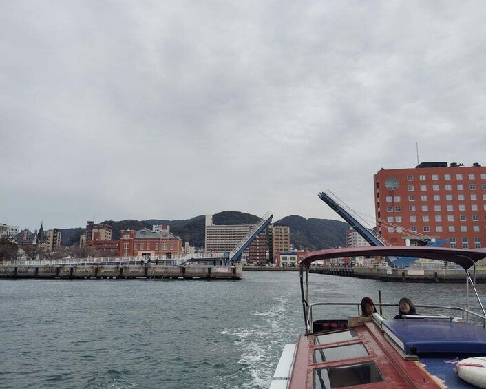 A boat on water with a cityscape in the background, including a bridge and buildings. 5