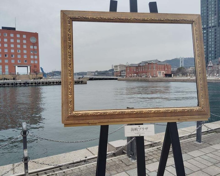 A framed picture on an easel by a waterfront with buildings in the background. 3