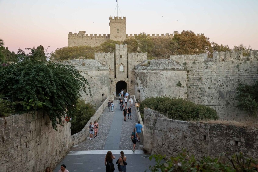 A historic stone castle with a central tower, a paved walkway, and visitors. 3