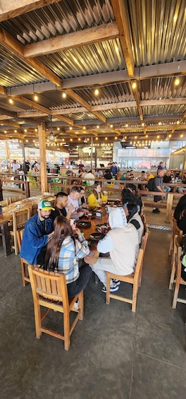 A group of people seated at a wooden table inside a restaurant with a high ceiling and exposed beams. 5