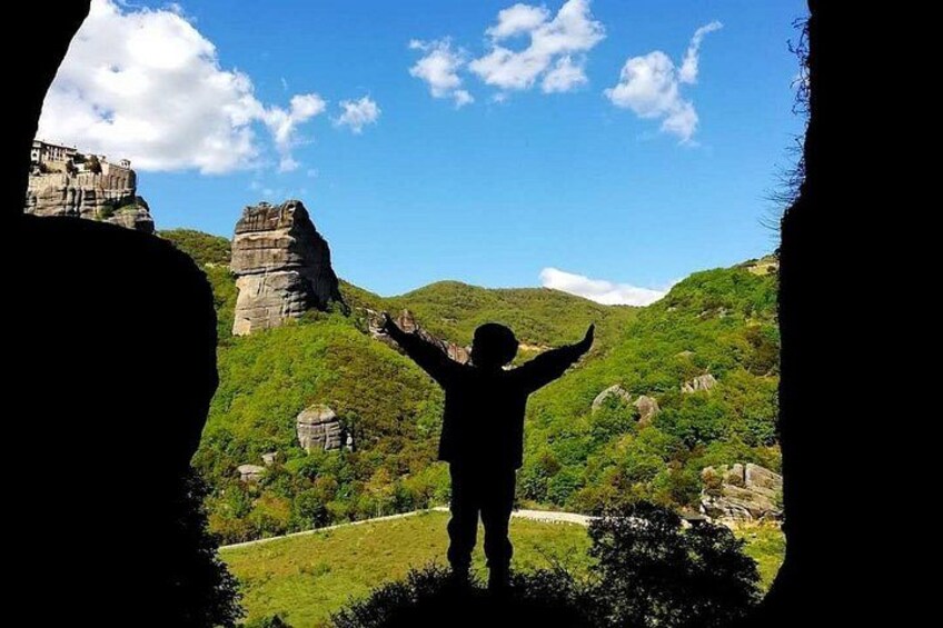 A person standing with arms raised in a natural landscape with rock formations and greenery. 4
