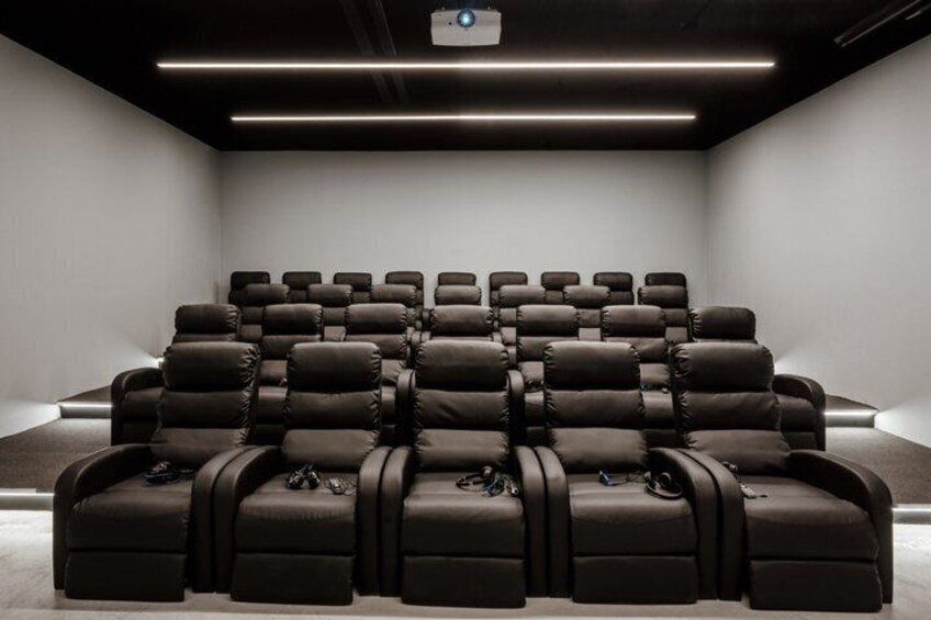 Une salle de cinéma moderne, dotée de rangées de fauteuils inclinables en cuir noir et d’un projecteur fixé au plafond. 5